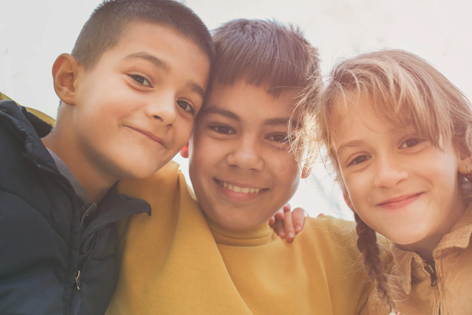 Group of smiling school-age children standing closely together outdoors.