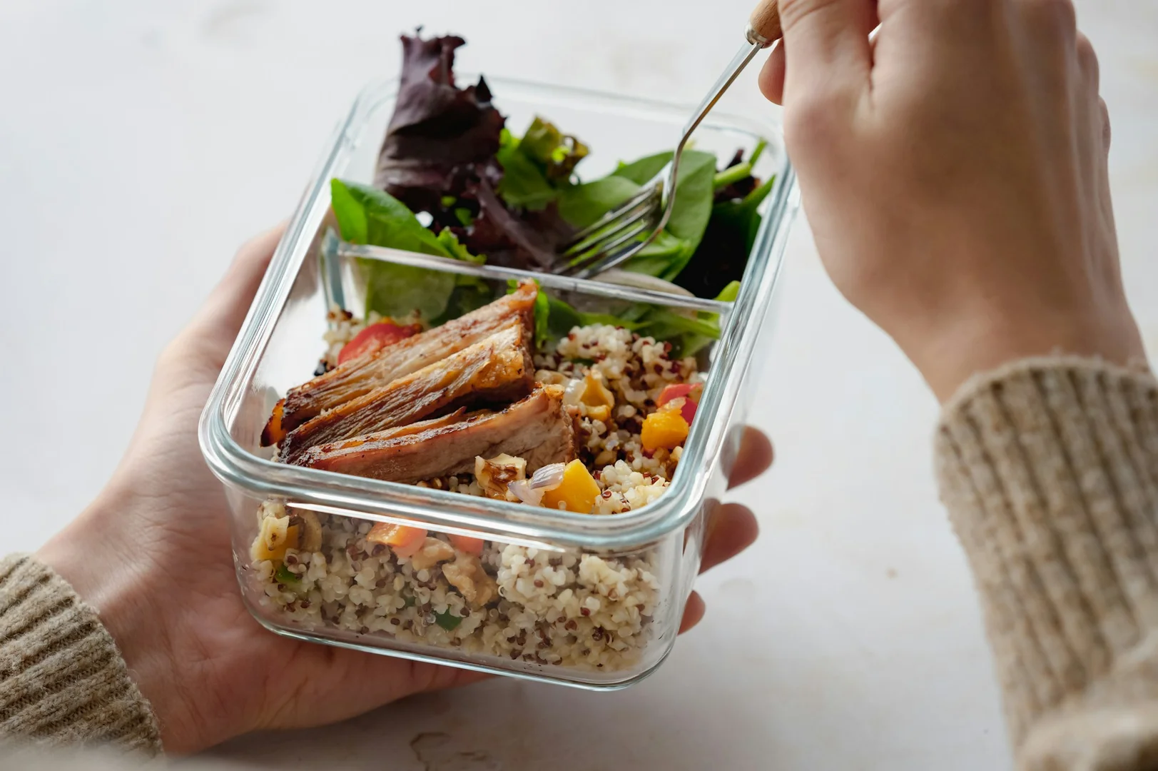 Close-up of a student holding a glass lunch container with quinoa, grilled chicken, and fresh greens.