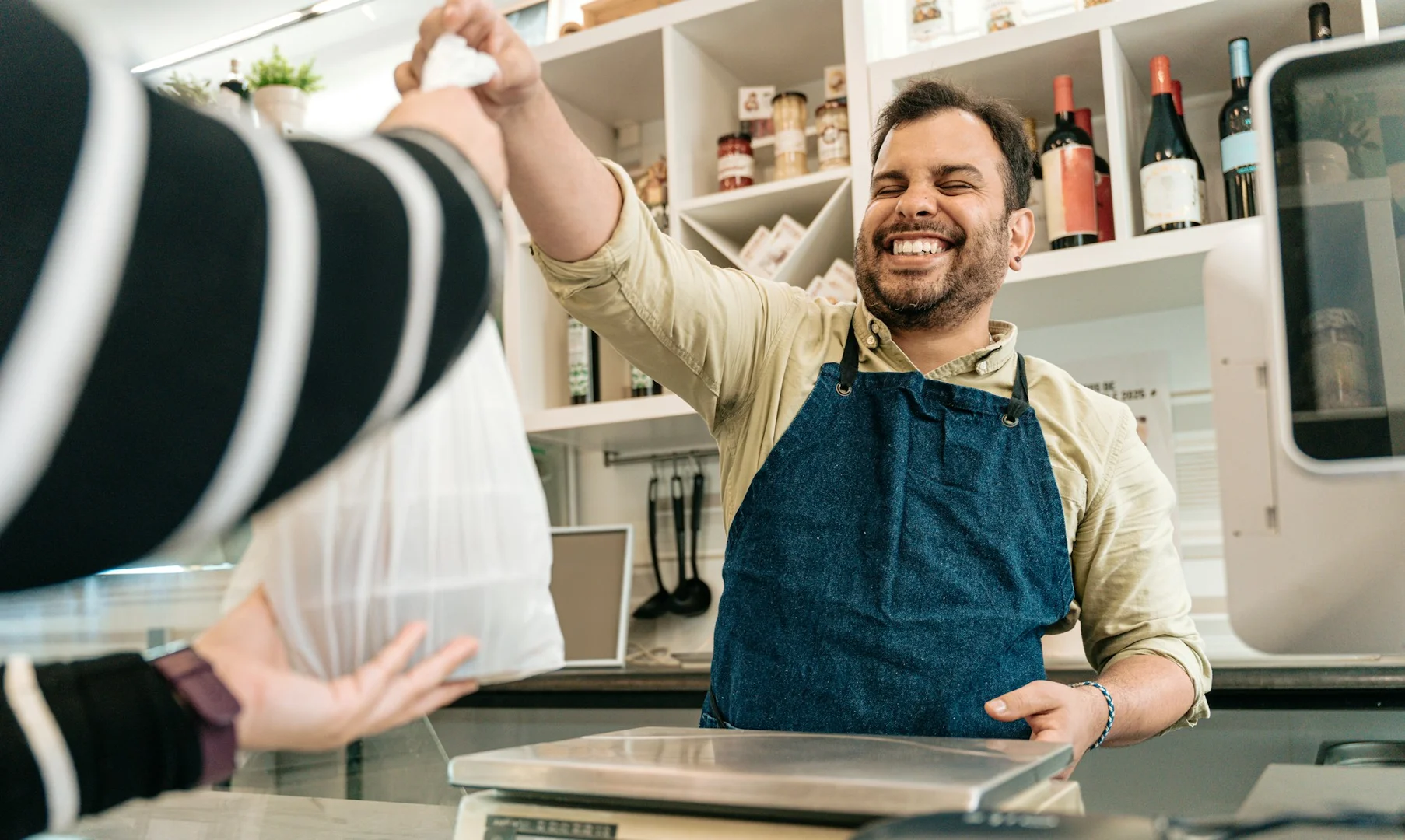 A smiling restaurant owner handing a takeout bag to a customer, symbolizing a local business partnership for school fundraising.