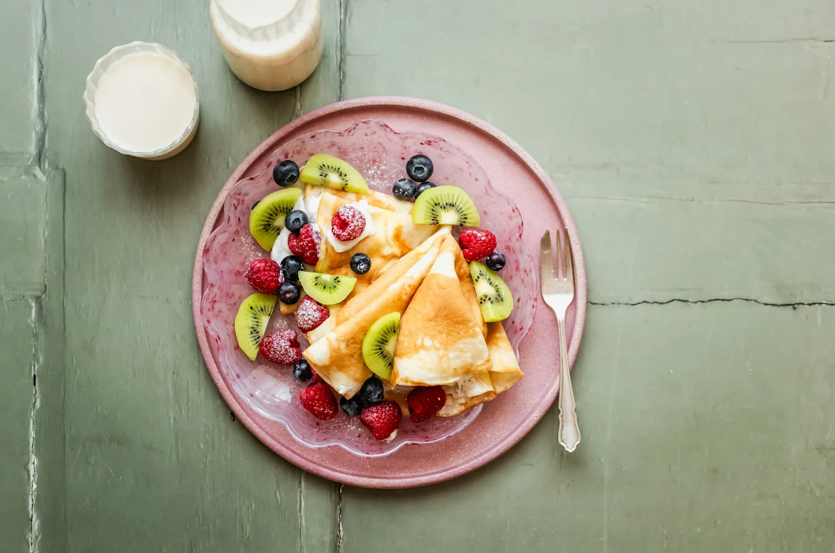 A plate of gluten-free crepes topped with fresh berries and kiwi, ideal for a healthy school hot lunch.