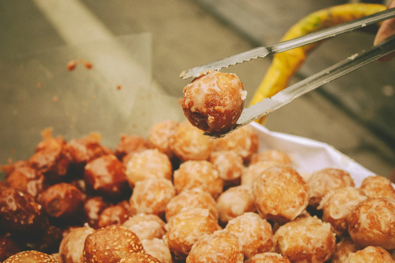 A pair of tongs holding a gluten-free meatball above a tray of freshly cooked meatballs.