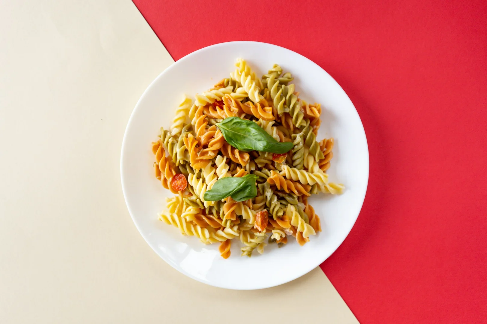 Gluten-free tri-colour pasta with basil and cherry tomatoes served on a white plate.