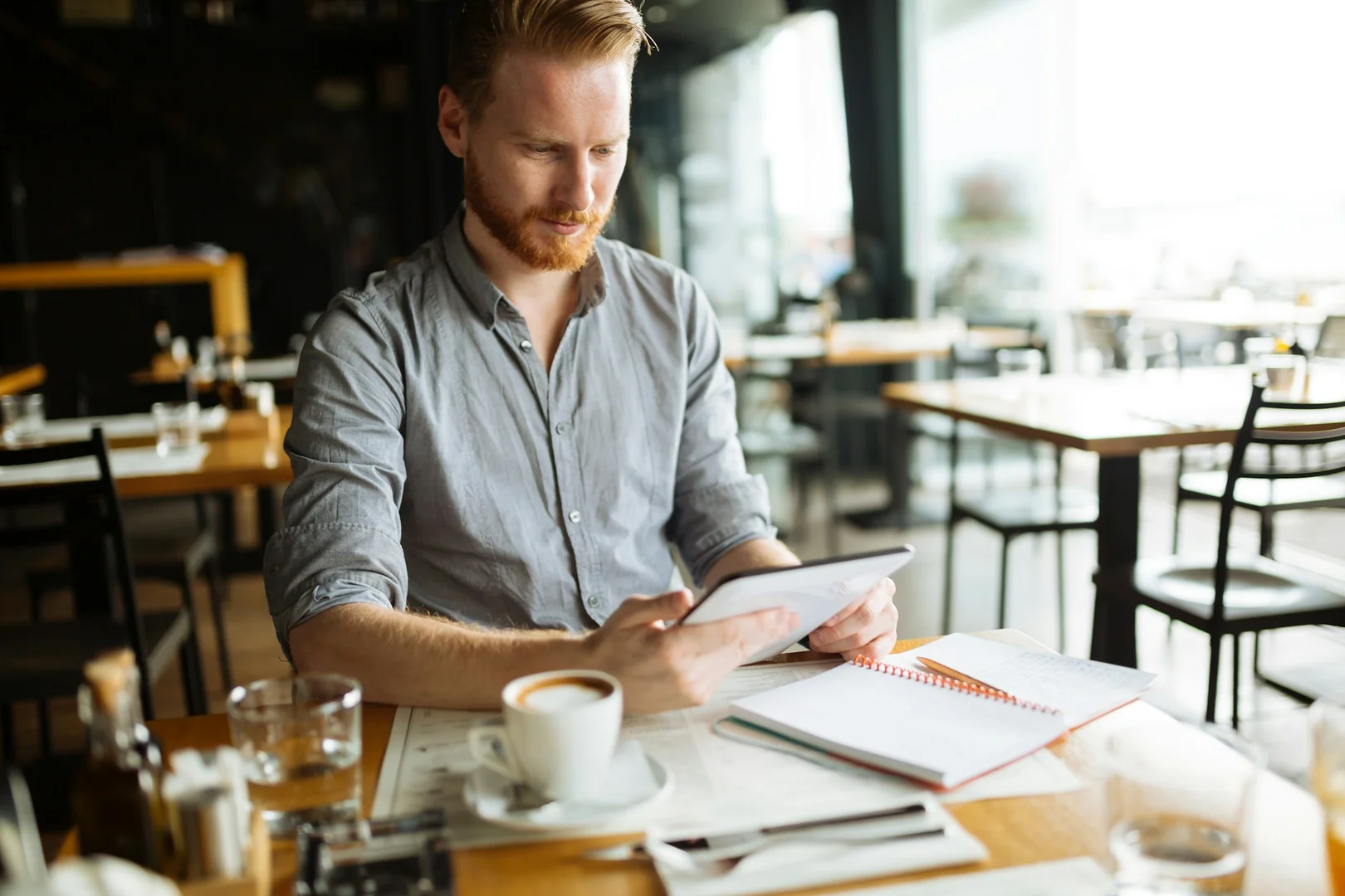 Restaurant owner reviewing notes and tablet while planning school lunch ordering and payment processes.